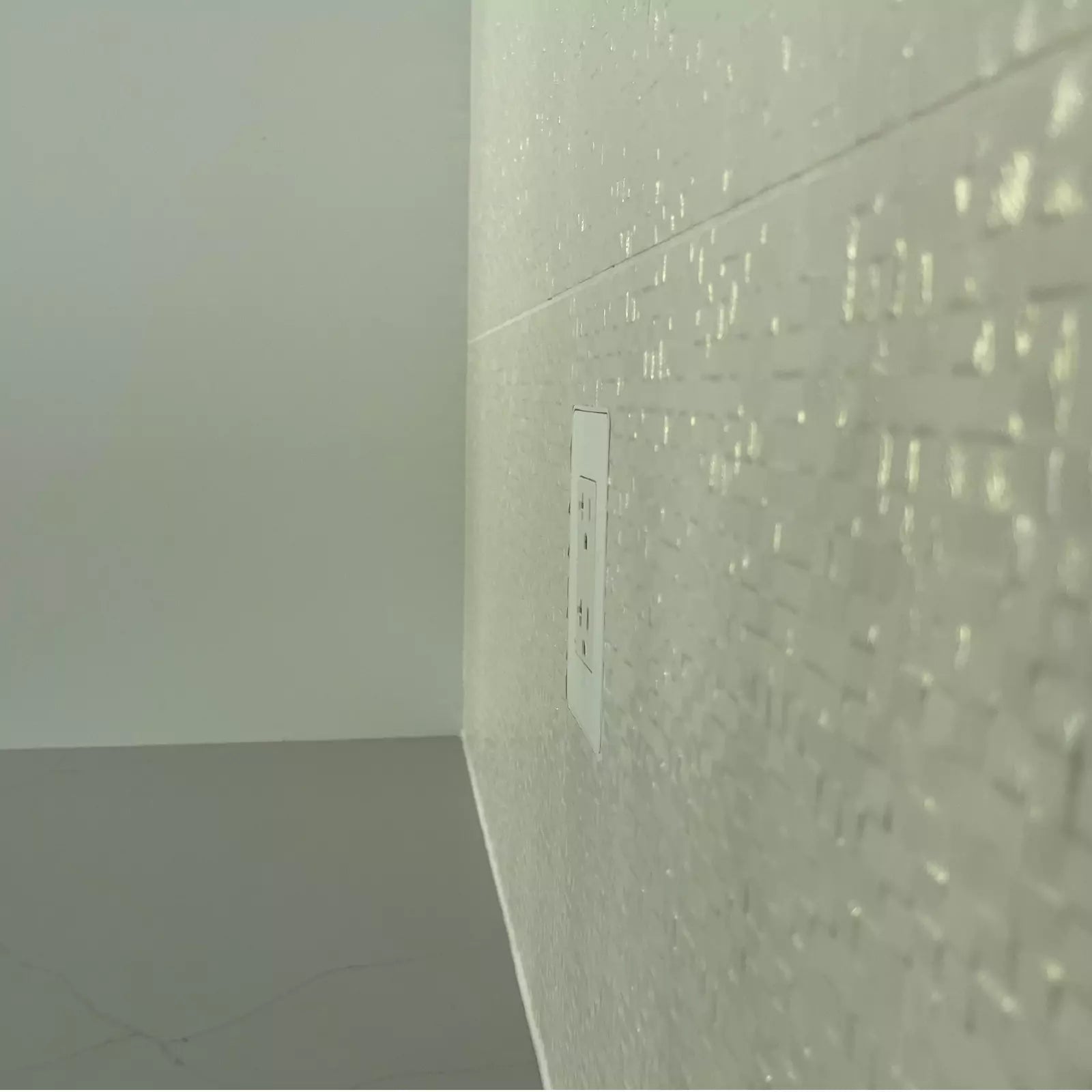 Close-up of a CONCEAL flush-mounted Decora outlet on a white textured tile backsplash