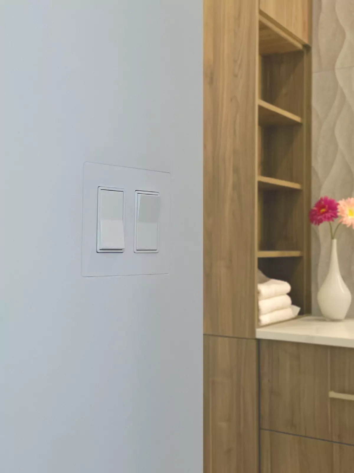 Two light switches flush-mounted using CONCEAL, seamlessly blending into the wall beside a modern vanity and round mirror