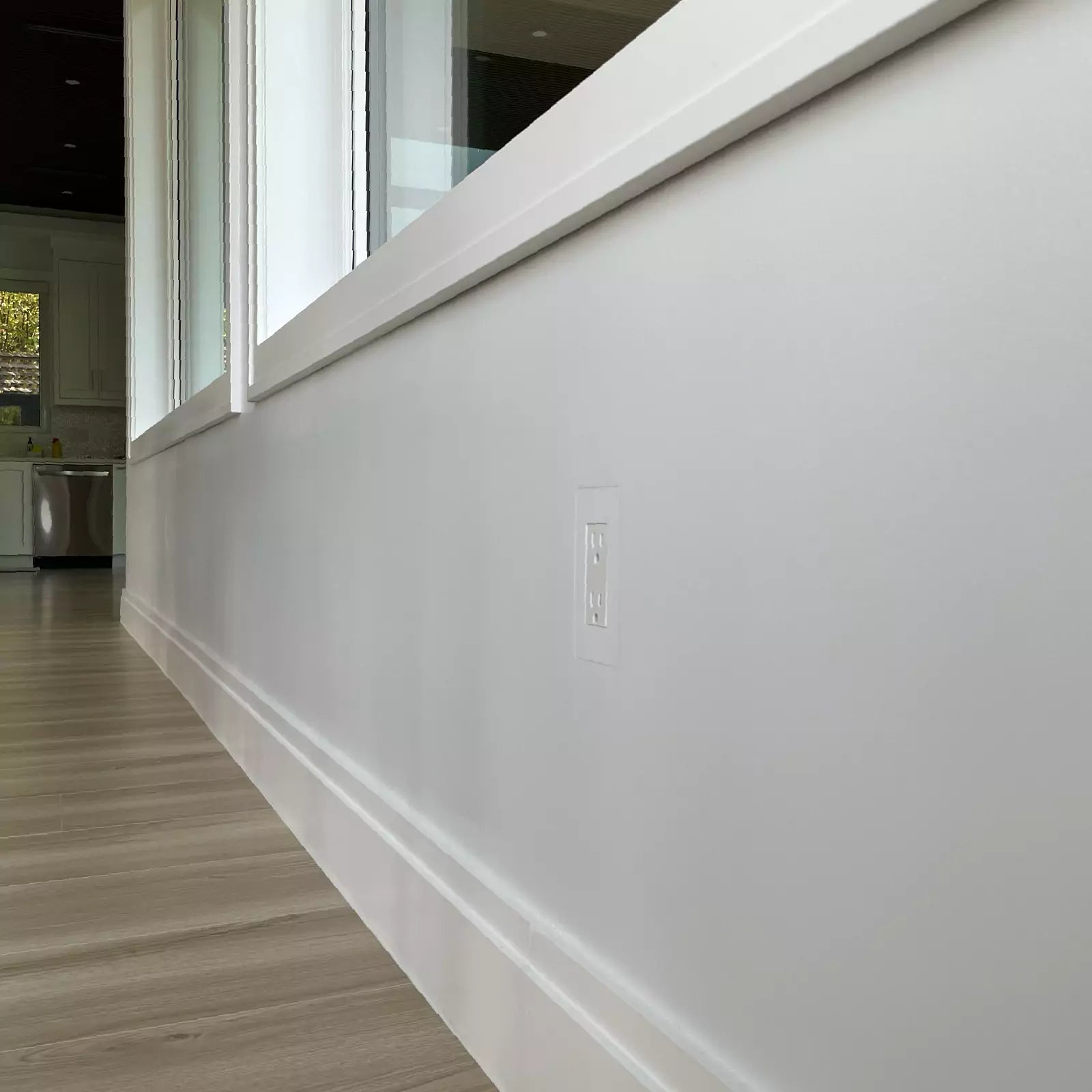 Close-up of a CONCEAL flush-mounted Decora outlet on a white wall with baseboards and large windows in a modern dining room