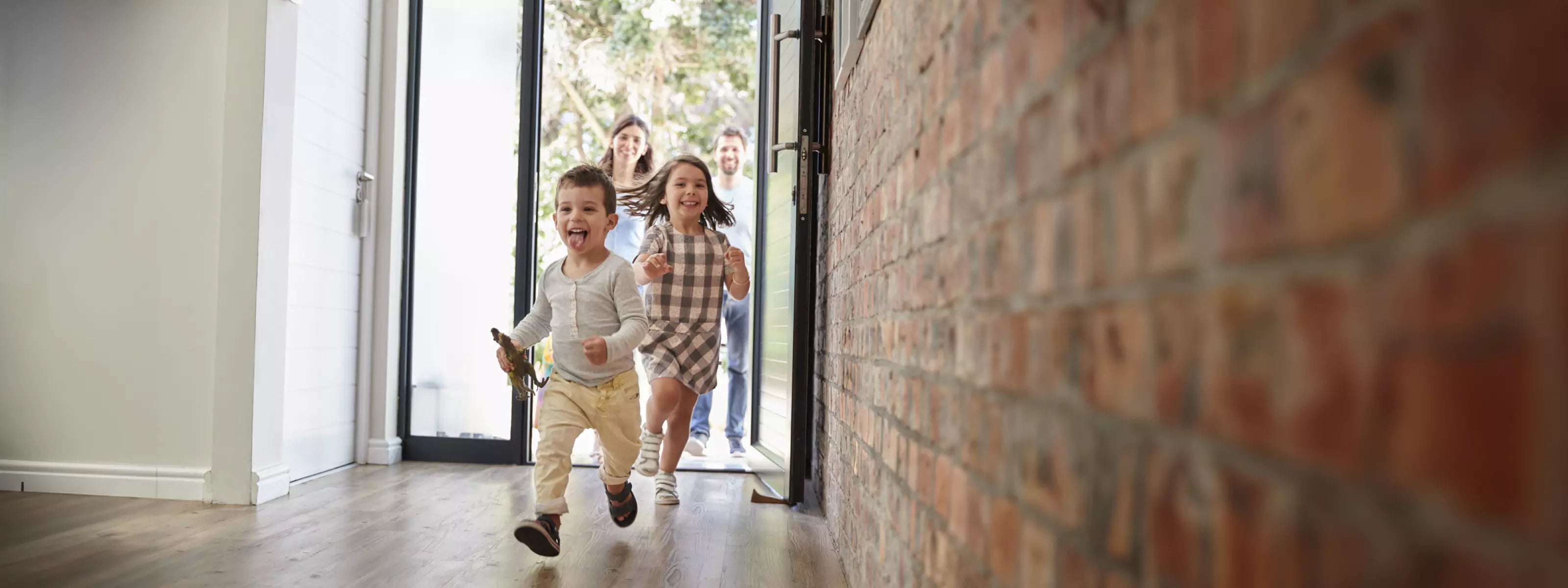 Two kids running happily inside through open front door as parents follow behind