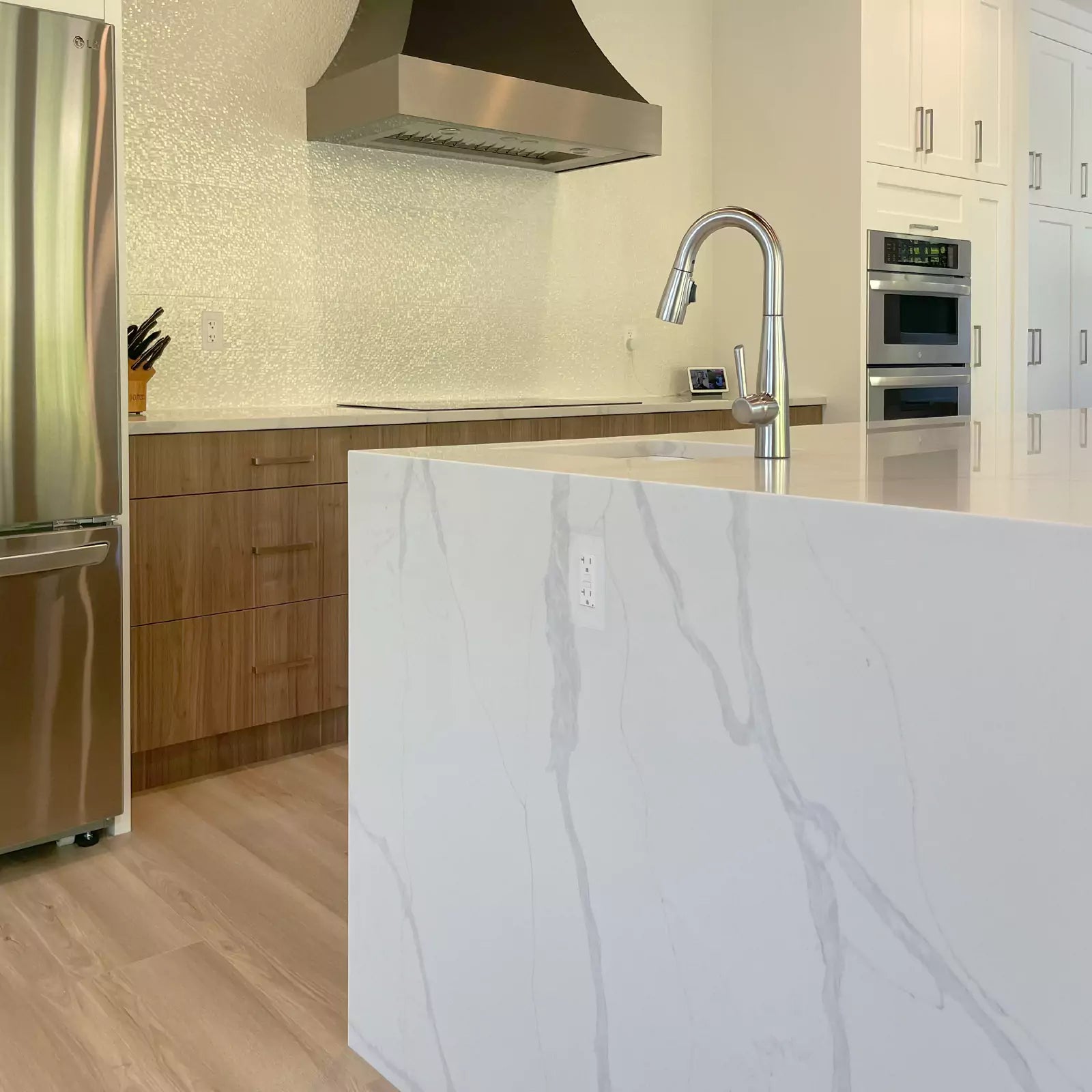 Modern kitchen with stainless steel appliances, wooden cabinets, and white marble island with CONCEAL flush-mounted outlets