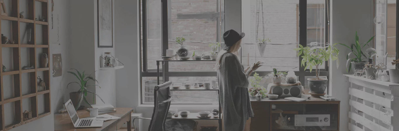 Modern home office with large windows, plants, and a woman working at her desk