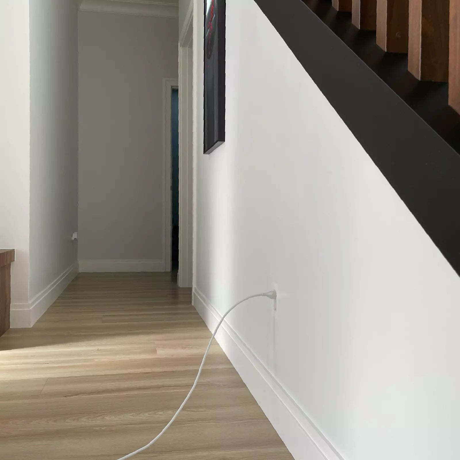 Modern interior with a white wall under a staircase and a CONCEAL flush-mounted outlet with a white power cord plugged in