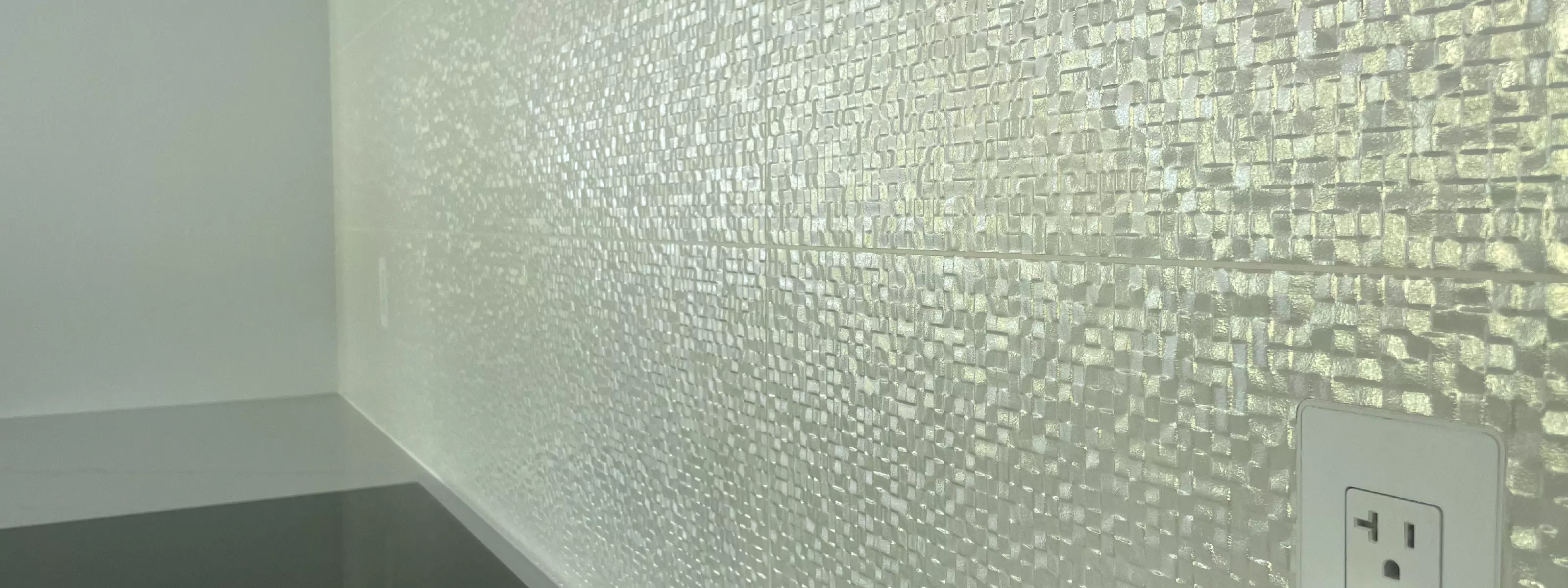 Flush-mounted kitchen outlet with CONCEAL system seamlessly integrated into textured glass tile backsplash above a countertop