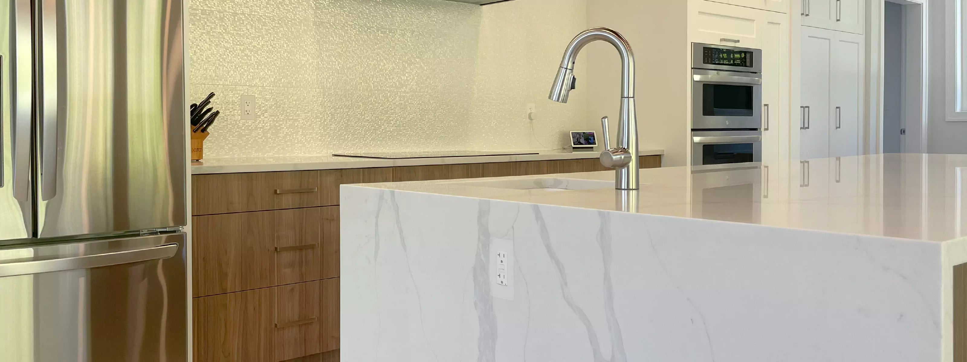 Modern kitchen with stainless steel appliances, wooden cabinets, and white marble island with CONCEAL flush-mounted outlets
