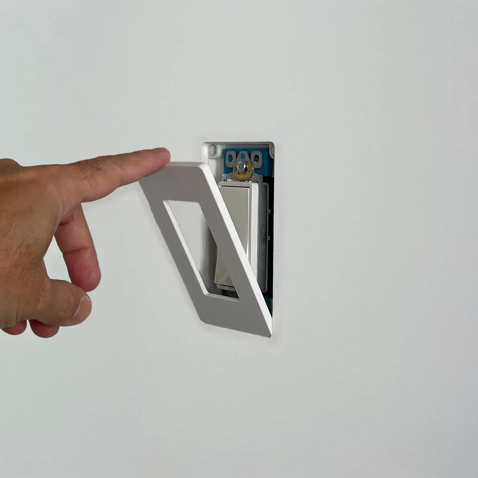 A hand attaching a CONCEAL magnetic wall plate over a Decora light switch flush-mounted on a white wall.