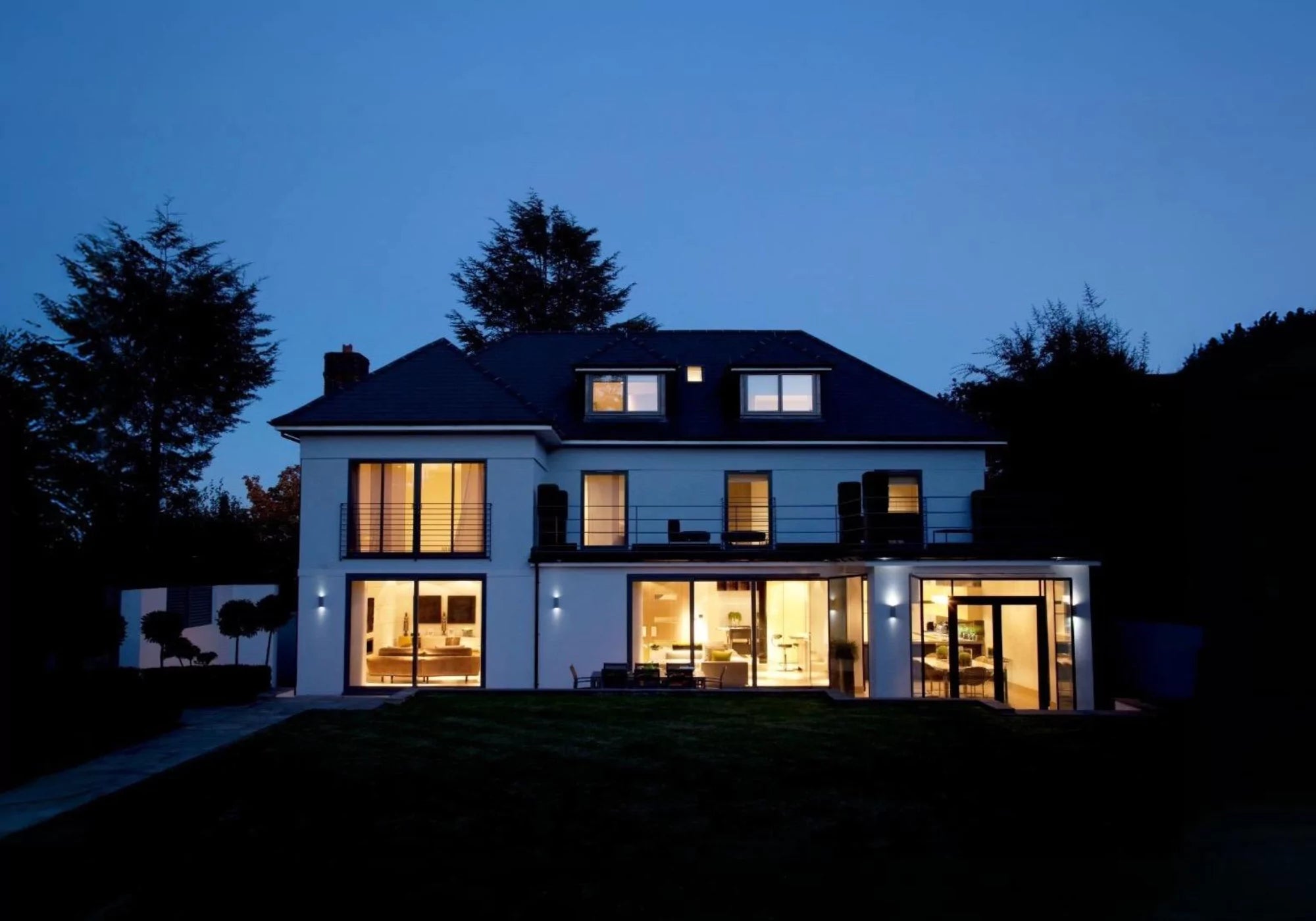 Modern two-story white stucco home at night with warm lights glowing, showcasing smart lighting automation