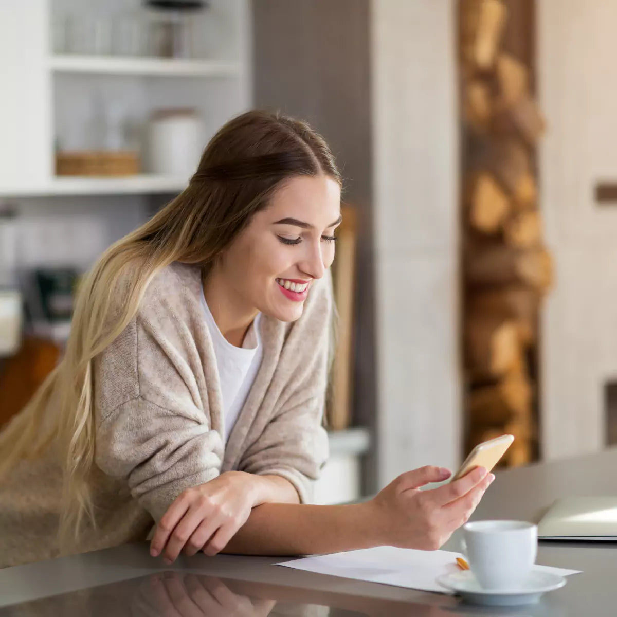 Smiling woman leaning on kitchen counter, controlling home lighting with smartphone
